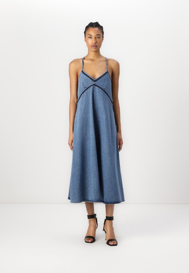 Denim midi-kjole med spaghetti stropper, med en v-hals, svarte sømceller og en løs passform som slutter under kneet.