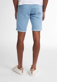 Pantalones cortos de mezclilla azul claro con dobladillos enrollados, que cuentan con dos bolsillos traseros y una textura suave. El calzado es blanco con acentos en beige.
