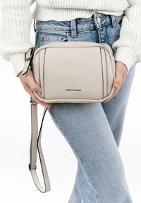 Borsa a tracolla color beige chiaro realizzata in pelle testurizzata. Presenta una chiusura con zip, un manico regolabile e un dettaglio con il nome del marchio in rilievo.