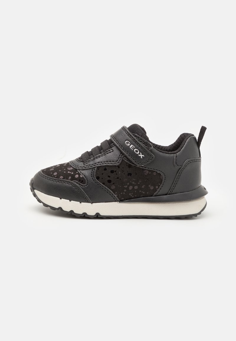 Baskets noires pour enfants en daim tacheté, bride en velcro étiquetée « GEOX » et semelle blanche sur fond clair uni.