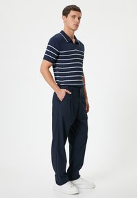 Polo de color marino con rayas horizontales blancas, de manga corta y con un diseño texturizado de canalé. Combinado con pantalones marinos y zapatillas blancas.