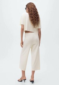 Top corto crema y pantalones anchos hechos de una tela suave y texturada. El conjunto presenta un corte en la espalda y se acompaña de sandalias de tacón negro.