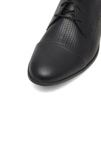 Černá kožená bota s tkaným vzorem na svršku, kulatou špičkou a hladkým kapesním dílem. Má tónované šněrování a plochou podrážku.