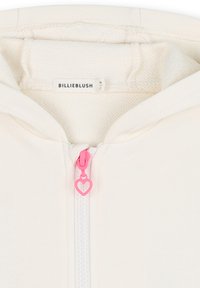 Lichtgekleurde rits-hoodie met een zachte textuur. Heeft een roze hartvormige ritshanger en een label met de tekst "BILLIEBLUSH."