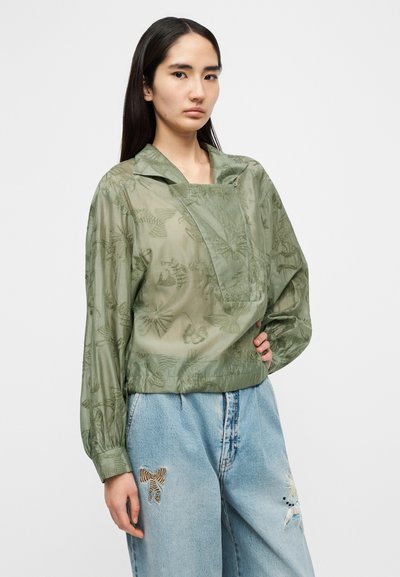 Ανοιχτό πράσινο διάφανο μπλουζάκι με κεντήματα από λουλούδια, γιακά και μακριά μανίκια, συνδυασμένο με φαρδιά τζιν παντελόνια που διαθέτουν διακοσμητικές επιδιορθώσεις.