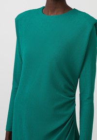 Abito teal con tessuto testurizzato, maniche lunghe e design strutturato delle spalle con dettagli arricciati sui lati.