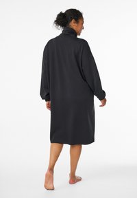 Svart oversized tröjdress med hög krage, långa ärmar och avslappnad passform, tillverkad av mjukt tyg. Inga synliga mönster eller accenter.