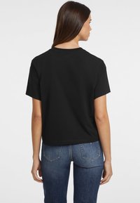 T-shirt noir en coton avec un design court, des manches courtes et un ourlet droit. Associé à un jean en denim bleu avec un design classique de poches arrières.