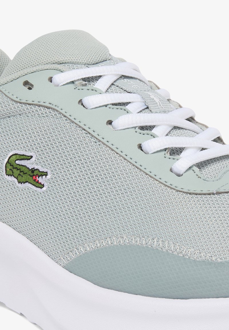 Baskets en mesh gris clair avec lacets blancs, broderie du logo crocodile de Lacoste et semelle en caoutchouc blanche.