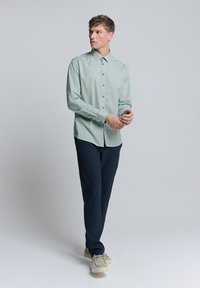 Lichtgroen overhemd met lange mouwen en een geometrisch patroon, met knoopsluiting en een button-down kraag, gedragen met marineblauwe broek en beige schoenen. Glad textuur, nauwsluitende pasvorm.