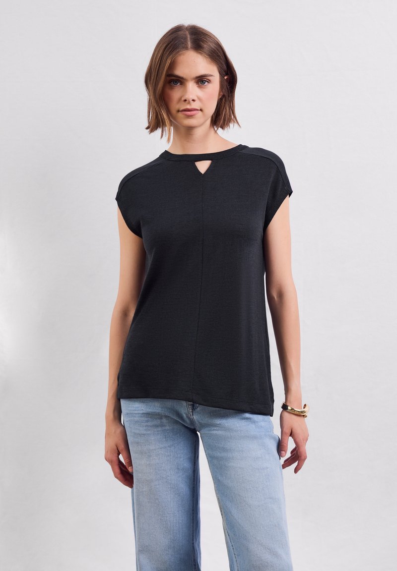 Černý top s krátkým rukávem a výstřihem ve tvaru klíčové dírky, jemná textura a volný střih, spárovaný s celkově modrými širokými džínami.