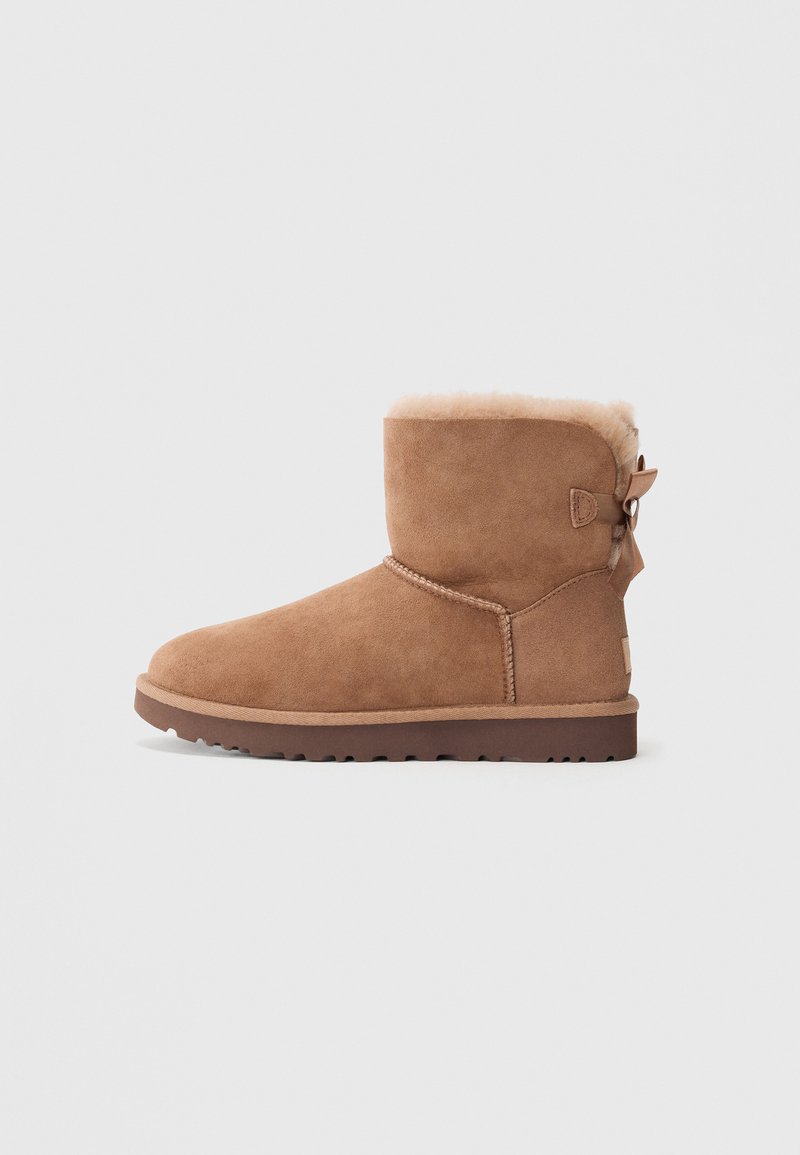 Brown suede ankle boot with a soft fur lining, rounded toe, and a small bow accent at the back; thick rubber sole with traction.
