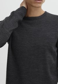 Pull en maille gris foncé avec un col rond et des poignets côtelés. Le tissu semble doux avec une texture subtile et un design léger.