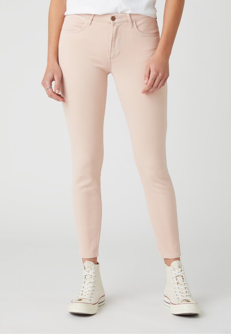 Jean skinny rose clair avec un tissu lisse et légèrement extensible, design à cinq poches et fermeture par un seul bouton à la taille.