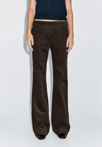 Bruine fluwelen broek met een uitlopende pijp en verticale ribbelstructuur, hoge taille en zijzakken, gecombineerd met een donkere, slim-fit top.