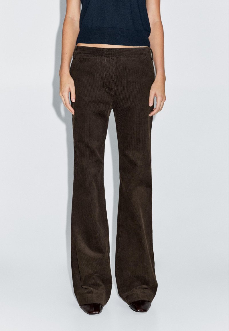 Bruine fluwelen broek met een uitlopende pijp en verticale ribbelstructuur, hoge taille en zijzakken, gecombineerd met een donkere, slim-fit top.