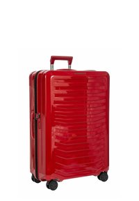 Valigia rigida rossa con un design elegante, linee orizzontali testurizzate, manico telescopico e quattro ruote nere per una facile manovrabilità.