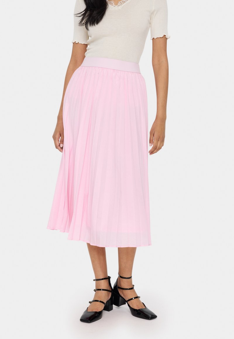 Jupe midi plissée rose clair avec une taille élastique, associée à des chaussures à talons blocs striées noires. Tissu lisse et texturé.