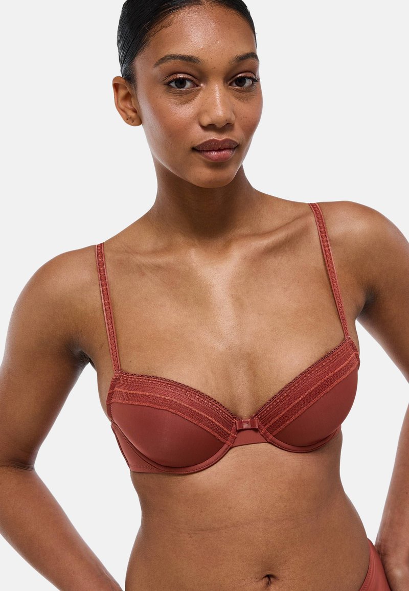 Soutien-gorge rembourré rouge avec bordure en dentelle, bretelles réglables et finition lisse. Doté d'un fermoir central et d'une conception structurée.
