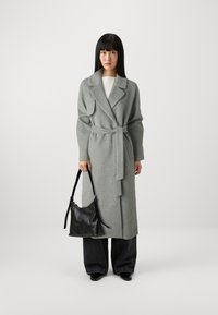 Gray wool wrap coat with a wide collar and belt, paired with black leather handbag. Model wears wide-leg dark jeans and patent shoes.