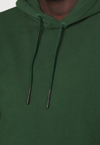 Groene hoodie gemaakt van een zachte katoenmix met een capuchon met trekkoorden. Voorzien van zwarte aglets aan de trekkoorden en een gladde textuur.
