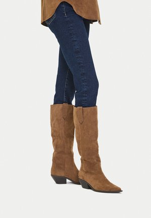 Braune Veloursleder-Cowboystiefel mit spitzer Zehenpartie und niedrigem, gestapeltem Absatz, mit seitlichen Akzenten am Schaft und glatter Textur.