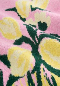 Vaaleanpunaista kudottua kangasta, jossa suuria keltaisia kukkakuvioita ja vihreitä korostuksia. Pehmeä rakenne, jossa näkyvät kuidut, luo kodikkaan ilmeen.