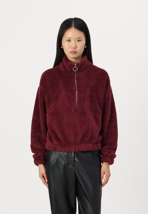 Burgunderfarget fleece genser med høyt krage, halv glidelås foran, ribbede mansjetter og elastisk midje. Strukturert stoff med synlige sømmer.