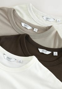 Neljä pyöreäkaulaista T-paitaa värissä beige, vaaleanharmaa, tummanruskea ja valkoinen, jokaisessa merkintä "Next" ja koko medium.