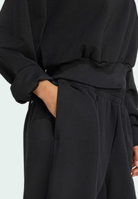 Ensemble de sweatshirt et pantalon noirs, doté d'une taille côtelée, d'une texture douce et de poches latérales avec un détail de poignet élastiqué.