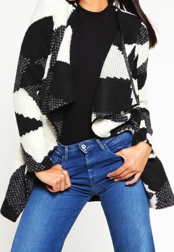 Cardigan a maglia con motivo geometrico in bianco e nero, aperto davanti, indossato sopra una maglietta nera e jeans blu. Tessuto testurizzato con una vestibilità comoda.