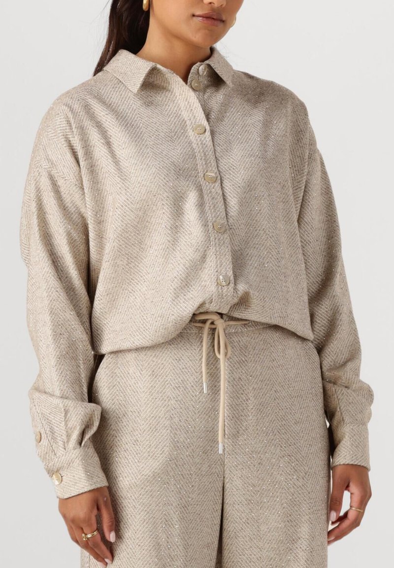 Beige herringbone patroon shirt met een relaxte pasvorm, knoopsluiting en omgeslagen mouwen. Zachte textuur met subtiele glinsterende accenten.