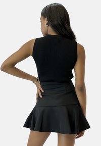 Top sin mangas de color negro con textura de canalé, combinado con una mini falda de vuelo negra. Tejido suave y diseño ajustado, cinturilla visible en la parte superior.