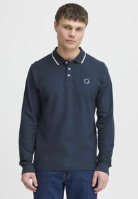 Marine langermet polo skjorte med en kontrasterende grå krage, tre-knappers placket og en liten hvit logo på brystet. Myk tekstur.