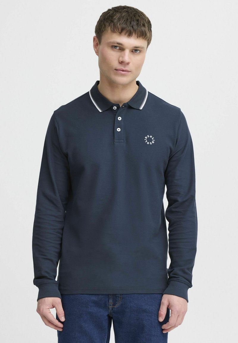 Marine langermet polo skjorte med en kontrasterende grå krage, tre-knappers placket og en liten hvit logo på brystet. Myk tekstur.
