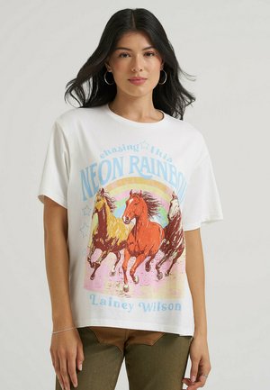 Donna che indossa una maglietta bianca con una grafica colorata di tre cavalli al galoppo e il testo "NEON RAINBOW" e "Lainey Wilson."