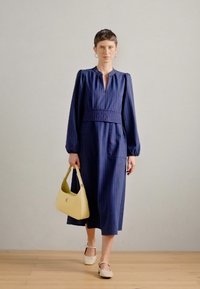 Sötétkék csíkos ruha hosszú labda ujjakkal, derékrésszel és két zsebbel, sárga kézitáskával és bézs cipővel párosítva.