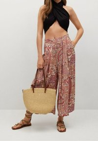 Palazzohousut, joissa on paisley-kuvio punaisen ja beigen sävyissä, yhdistettynä mustaan crop top -paitaan ja pyöreään olkilaukkuun ruskeilla hihnoilla.