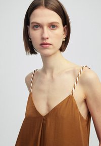 Vestido marrón sin mangas con escote en V, que cuenta con tirantes blancos retorcidos y un corte holgado con una textura sutil.