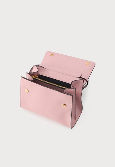Sac à main en cuir rose clair ouvert montrant l’intérieur avec une poche zippée dorée et des fermetures à boutons-pression sur un fond uni clair.