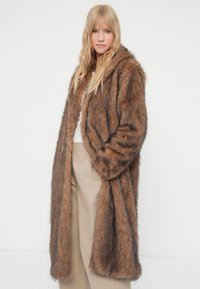 Cappotto in pelliccia sintetica marrone con cappuccio, maniche lunghe e vestibilità comoda. Presenta una texture morbida e sottili strisce più scure per un tocco di dettaglio in più.