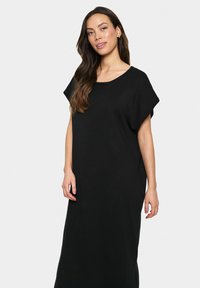 Fekete kötött ruha laza szabással, széles ujjakkal és kerek nyakkivágással. Hosszú, lebegő siluettája van. Sima textúra.