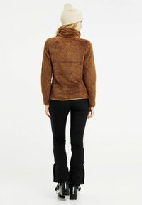 Bruine fleece pullover met een hoge kraag, gecombineerd met zwarte strakke broek en skischoenen. Zachte textuur met een ontspannen pasvorm.