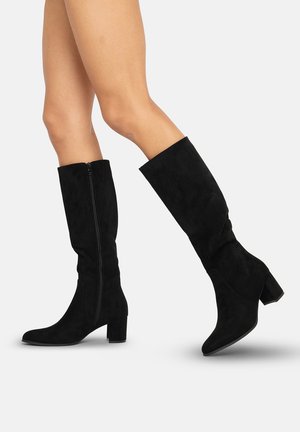 Botas altas de ante negras con tacón cuadrado, cremallera lateral y punta afilada. Textura suave con una silueta ajustada.