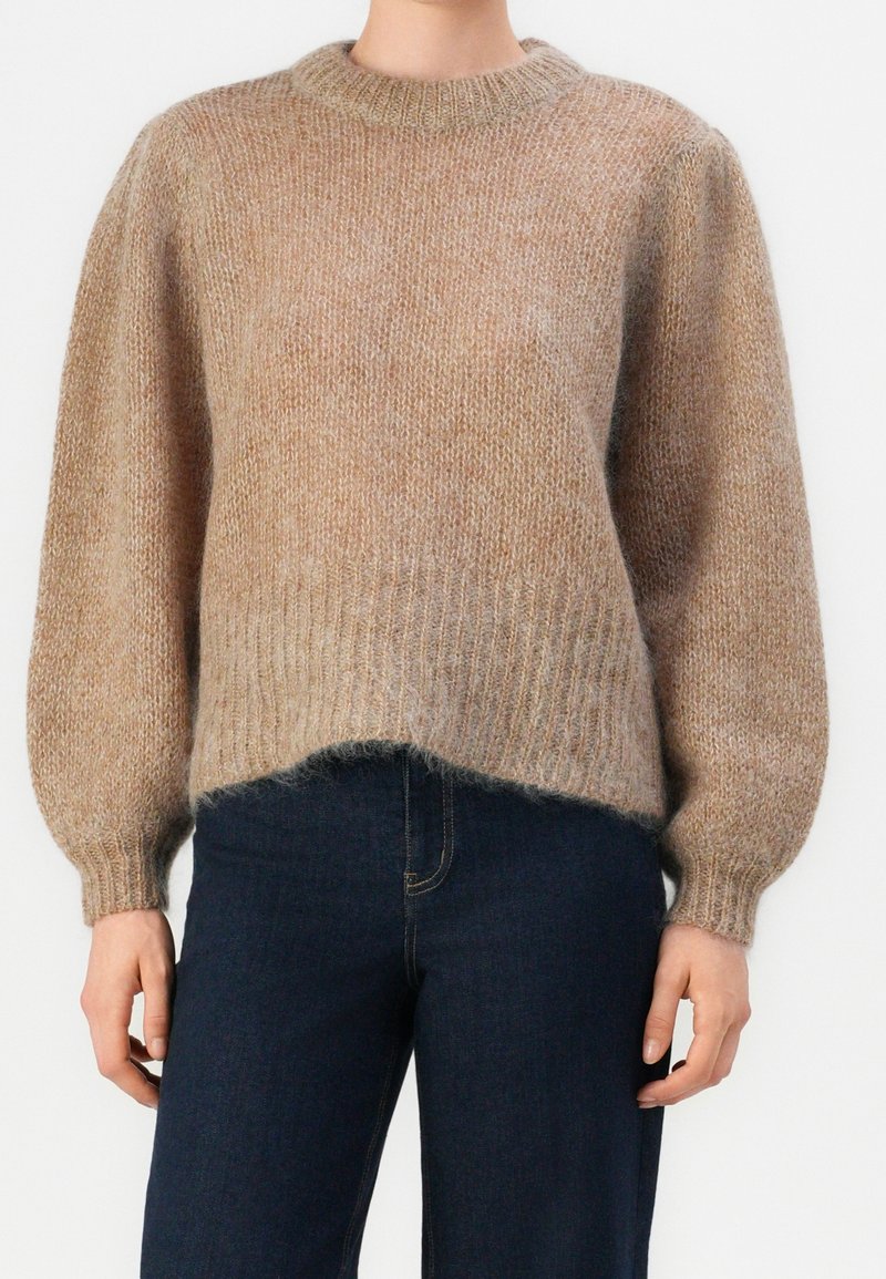 Pull en maille beige duveteuse avec col rond, poignets et ourlet côtelés, porté avec un pantalon taille haute bleu foncé.