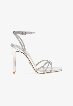 Silberne High-Heels Sandalen mit glänzender Oberfläche, ausgestattet mit mehreren überkreuzten Riemen, die mit Strasssteinen verziert sind, und einem Schnallenknöchelriemen.