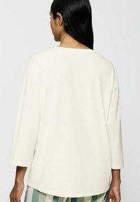 Długi rękaw, kremowy top o luźnym kroju. Posiada zaokrąglony dekolt oraz szwy na ramionach, które przechodzą w rękawy.