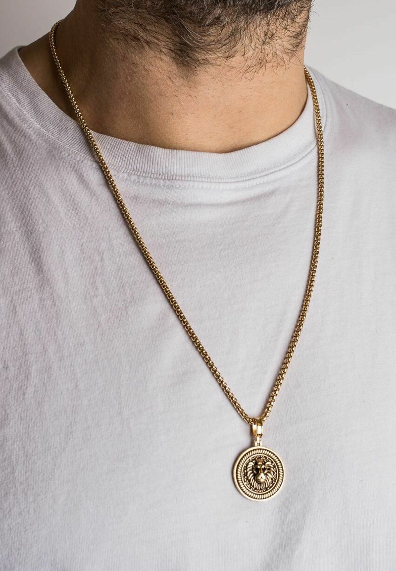 Goldkette mit einem kreisförmigen Löwenanhänger, der mit filigranen Details und einer strukturierten Oberfläche versehen ist, getragen über einem weißen Hemd.