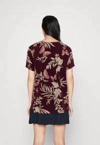 Bordowy t-shirt z krótkim rękawem z nadrukiem kwiatów i motyli w odcieniach beżu, z zaokrąglonym dołem i miękką teksturą.