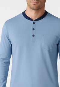 Camicia a maniche lunghe azzurro chiaro con collo navy, patta con cinque bottoni e taschino sul lato sinistro del petto; tessuto morbido e leggero.